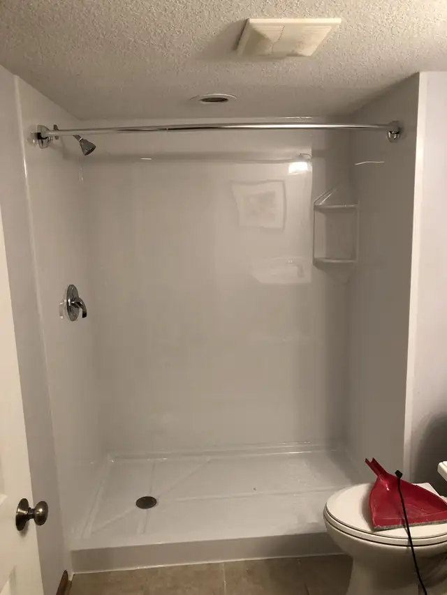 White panel walk-in shower with a built-in corner shelf and chrome valve